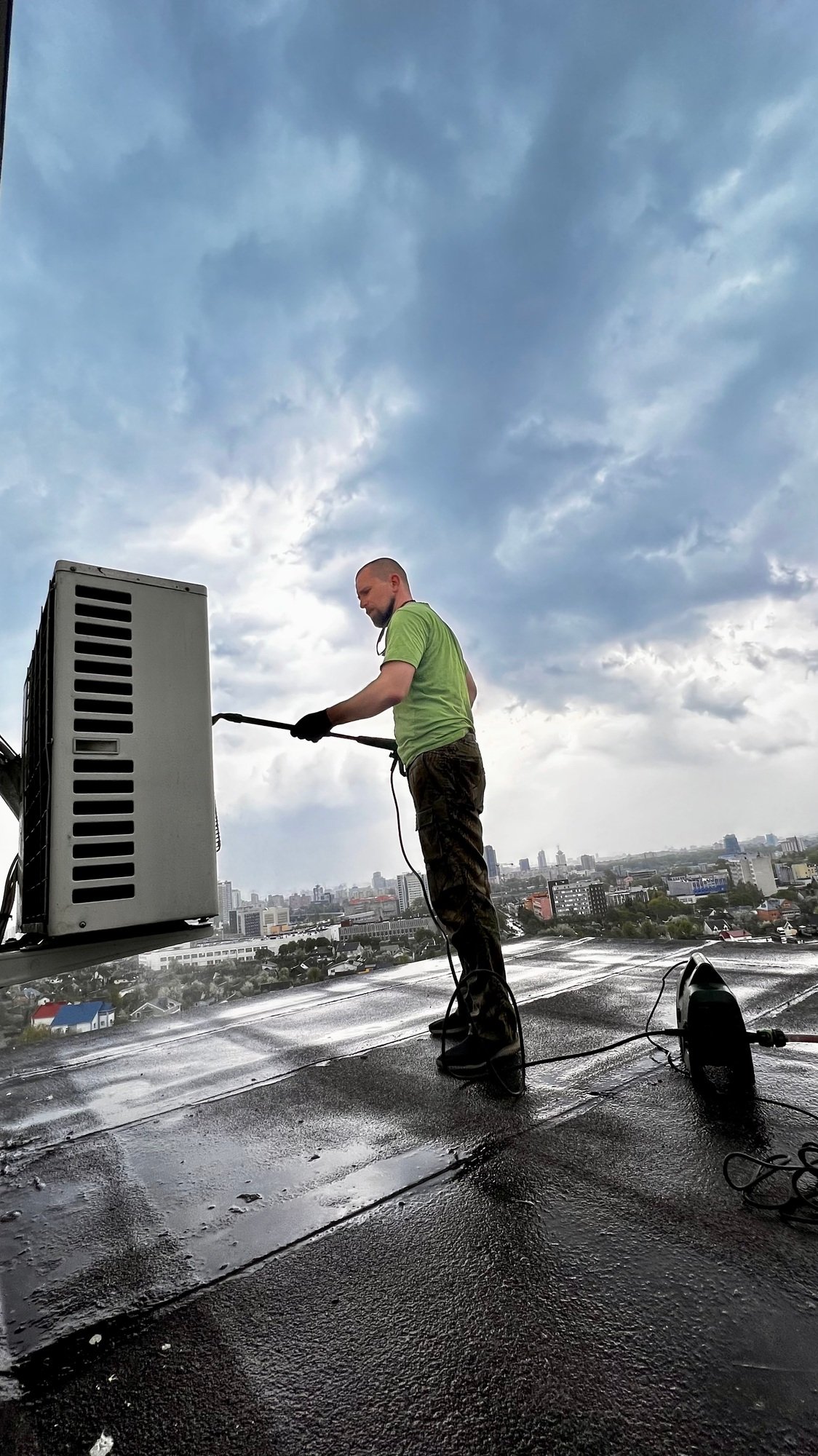 man washing the air conditioner on the roof